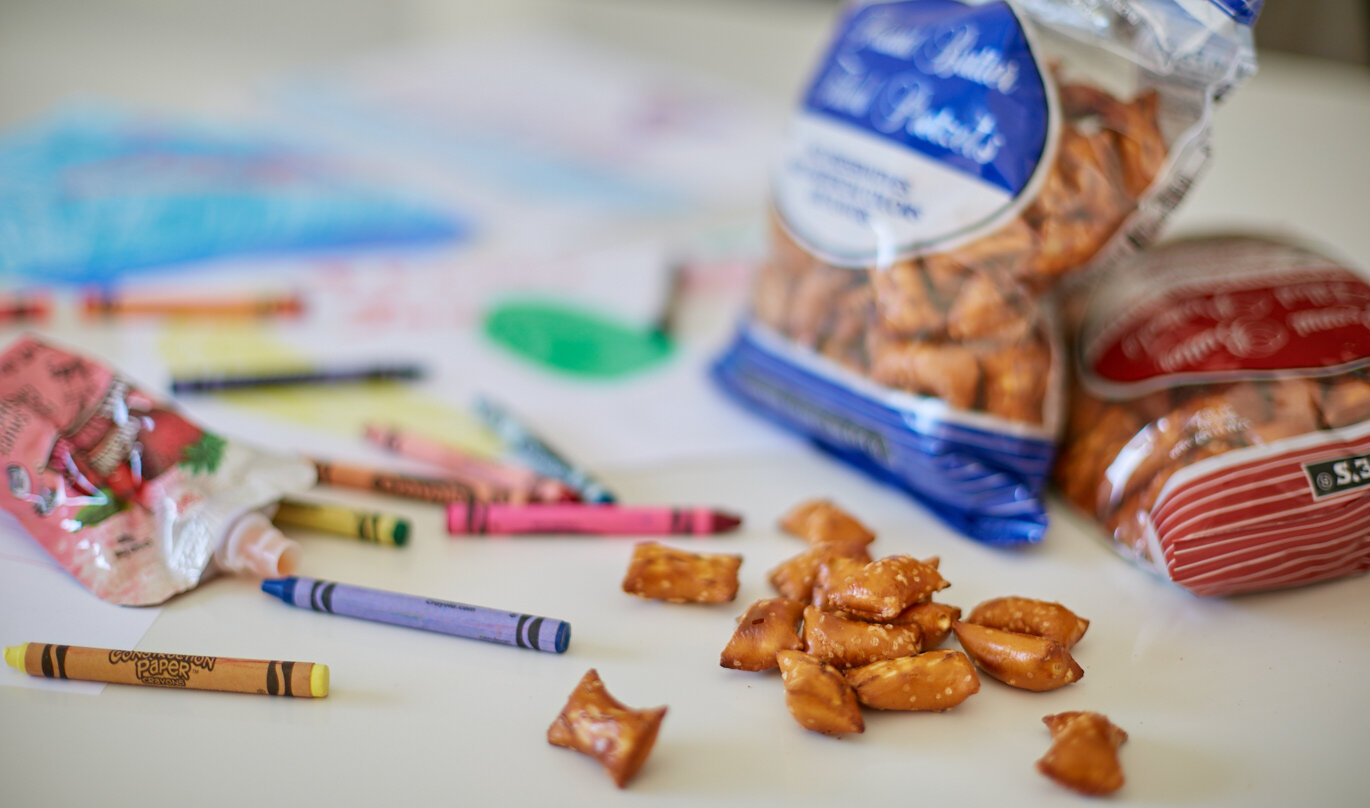 Trader Joe's Peanut Butter Pretzel Nuggets ; several on a surface next to crayons and drawing paper, colored drawings in background