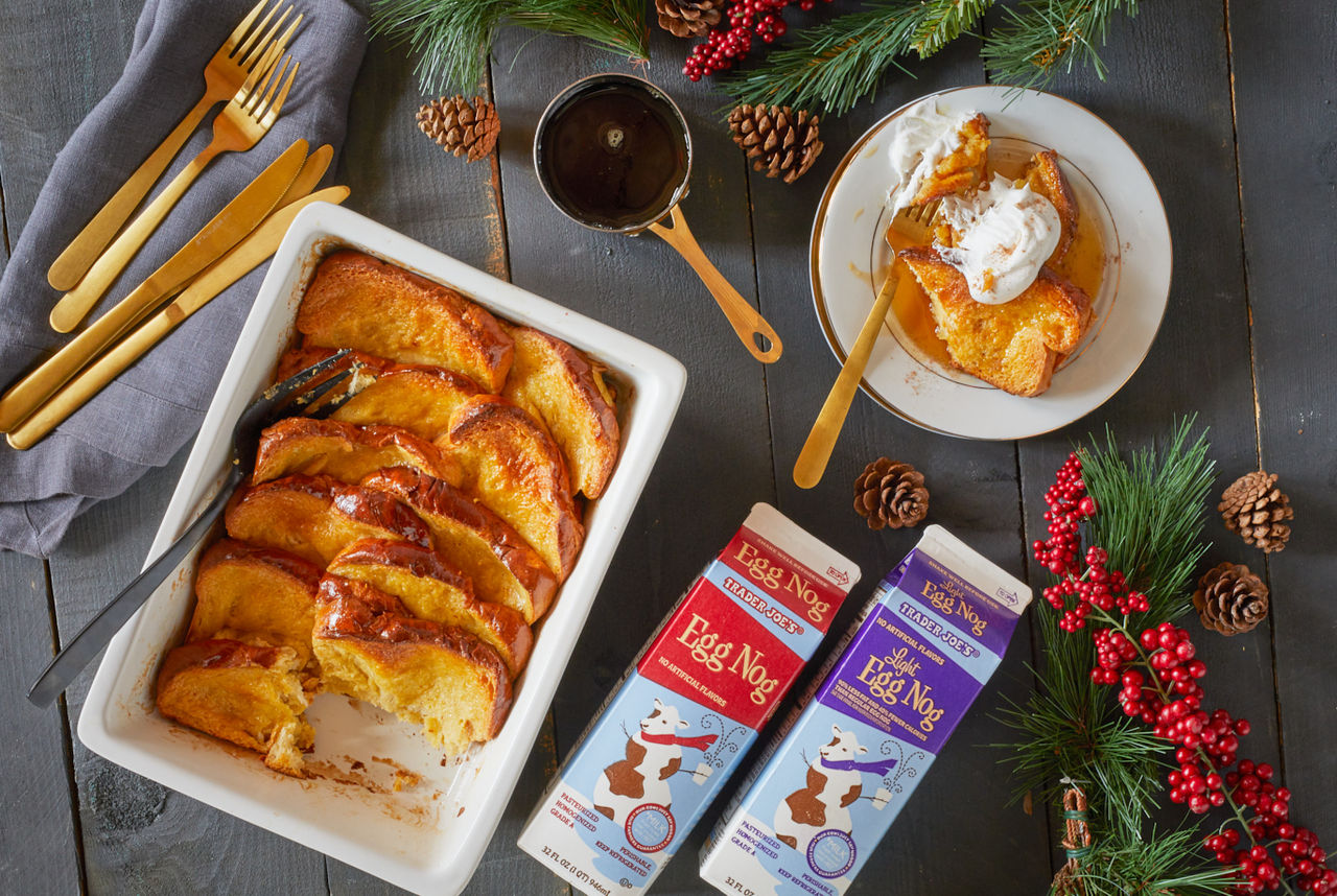 Trader Joe's Egg Nog & Light Egg Nog, used in recipe for Baked Egg Nog French Toast; shown in pan next to stack of plate and gold utensils, plate has a serving of french toast topped with syrup and whipped cream