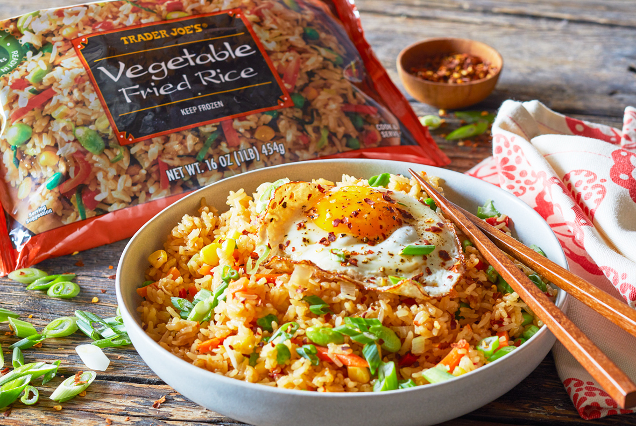 Trader Joe's Vegetable Fried Rice prepared in a bowl, topped with a fried egg, red pepper flakes and chopped green onions