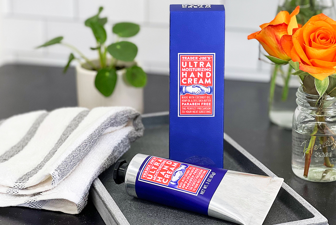 Trader Joe's Ultra Moisturizing Hand Cream rests on a bathroom counter, surrounded by flowers and a hand towel