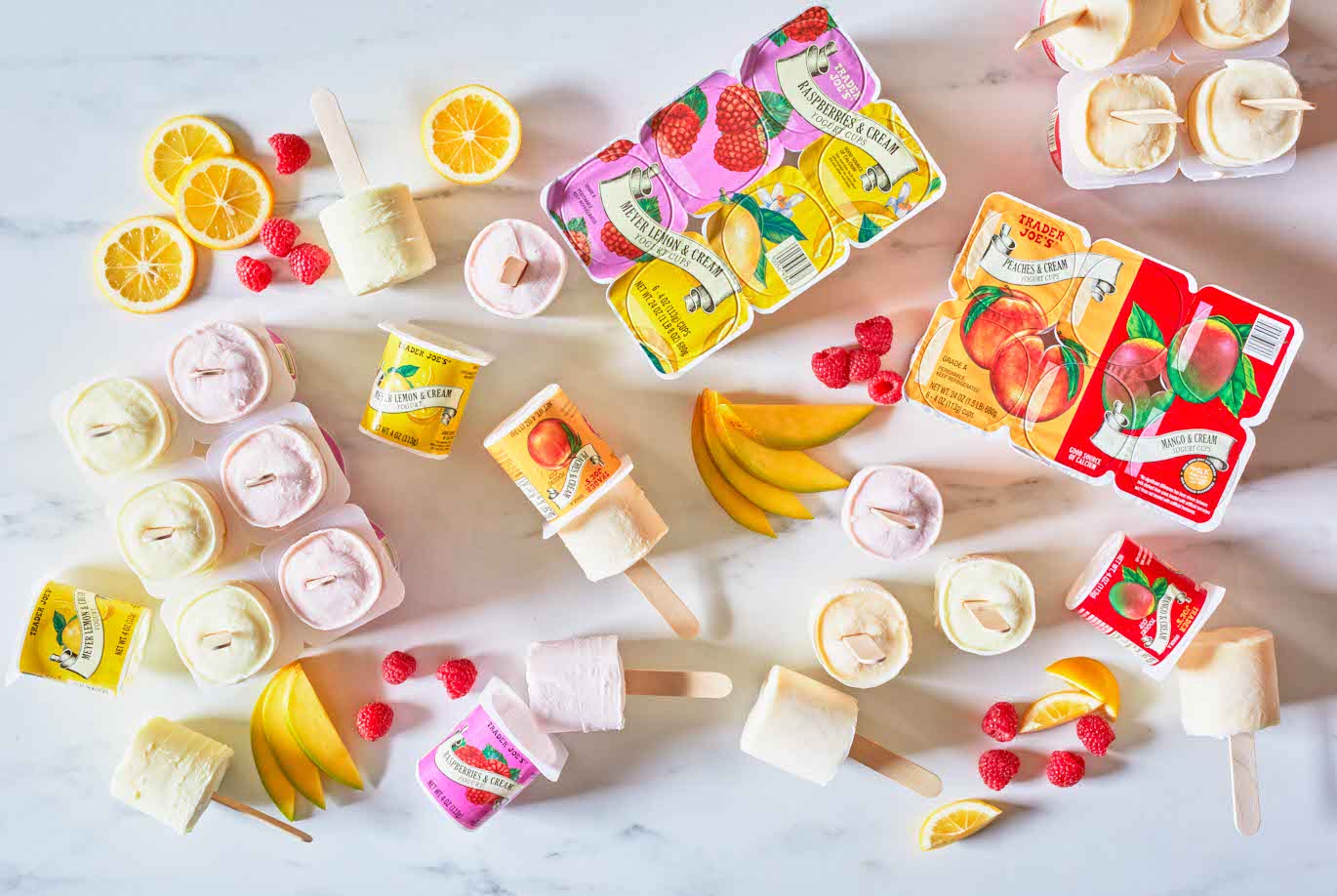 Trader Joe's Meyer Lemon, Raspberries & Cream and Peachs, Mango & Cream Yogurt Cups prepared as popsicles, some on surface with raspberries, meyer lemon and mango slices surrounding