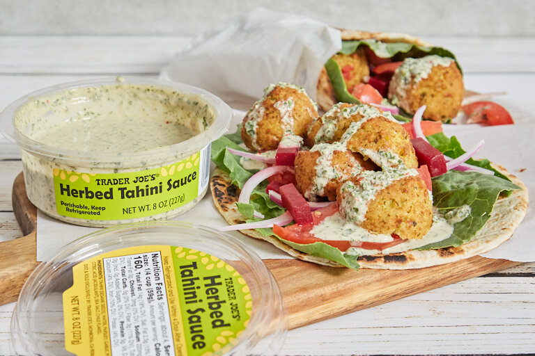 TJ's Herbed Tahini Sauce on a board next to a falafel wrap with the Herbed Tahini Sauce drizzled on top