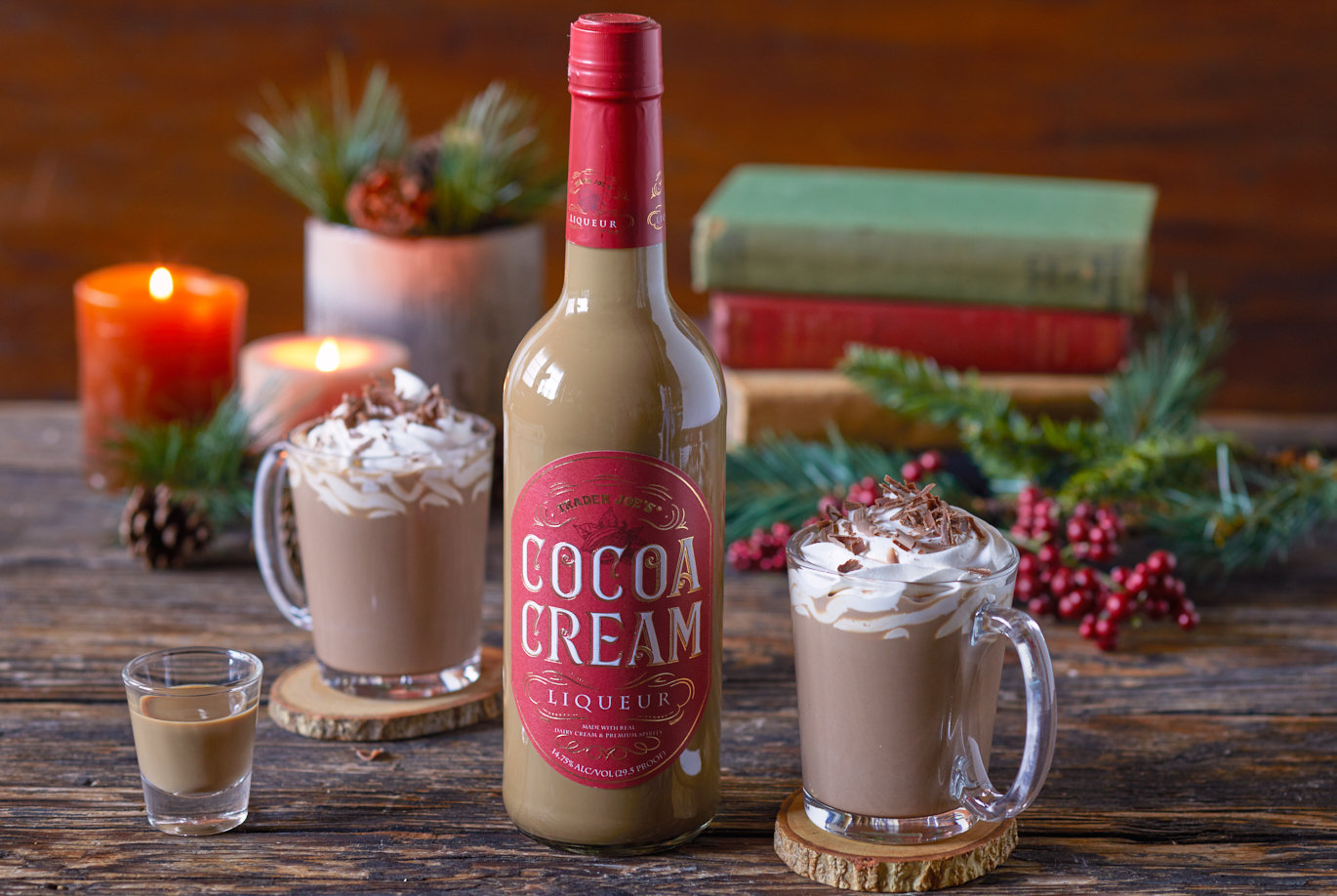 Trader Joe's Cocoa Cream Liqueur; shown in two glass mugs with hot cocoa & Cocoa Cream Liqueur, topped with whipped cream and chocolate shavings; moody wood backgound with candelight