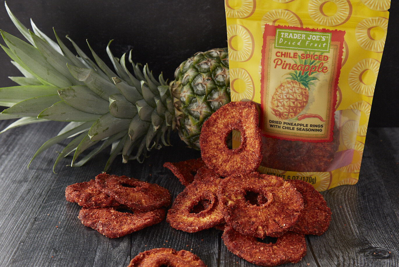 TJ's Chile Spiced Pineapple pieces on a dark surface, a whole pineapple in the background