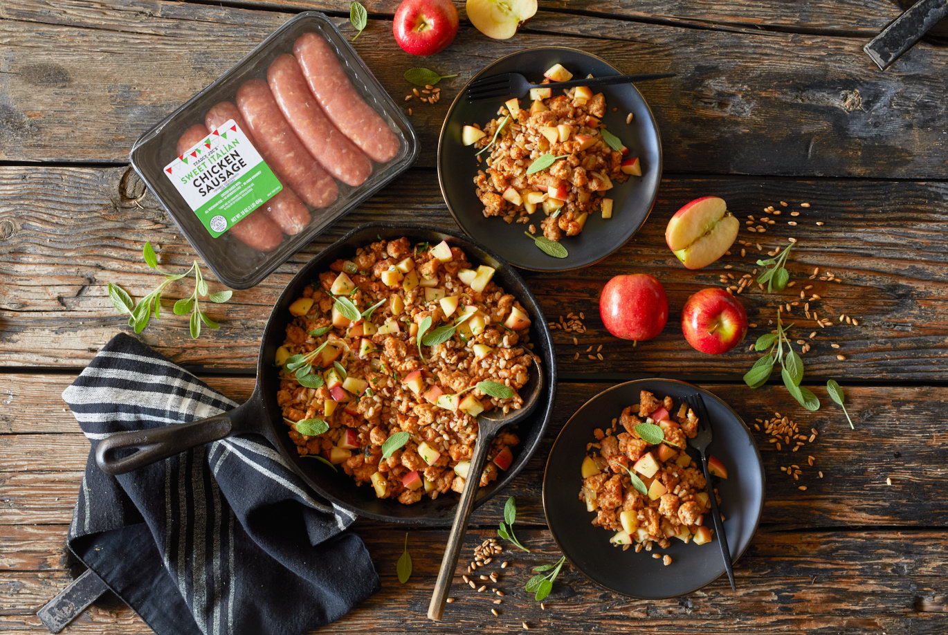 Trader Joe's Sweet Italian Chicekn Sausage used in recipe for Farro with Chicken Sausage; served in a cast iron skillet and two plates, dried farro, apples and sage leaves on surface