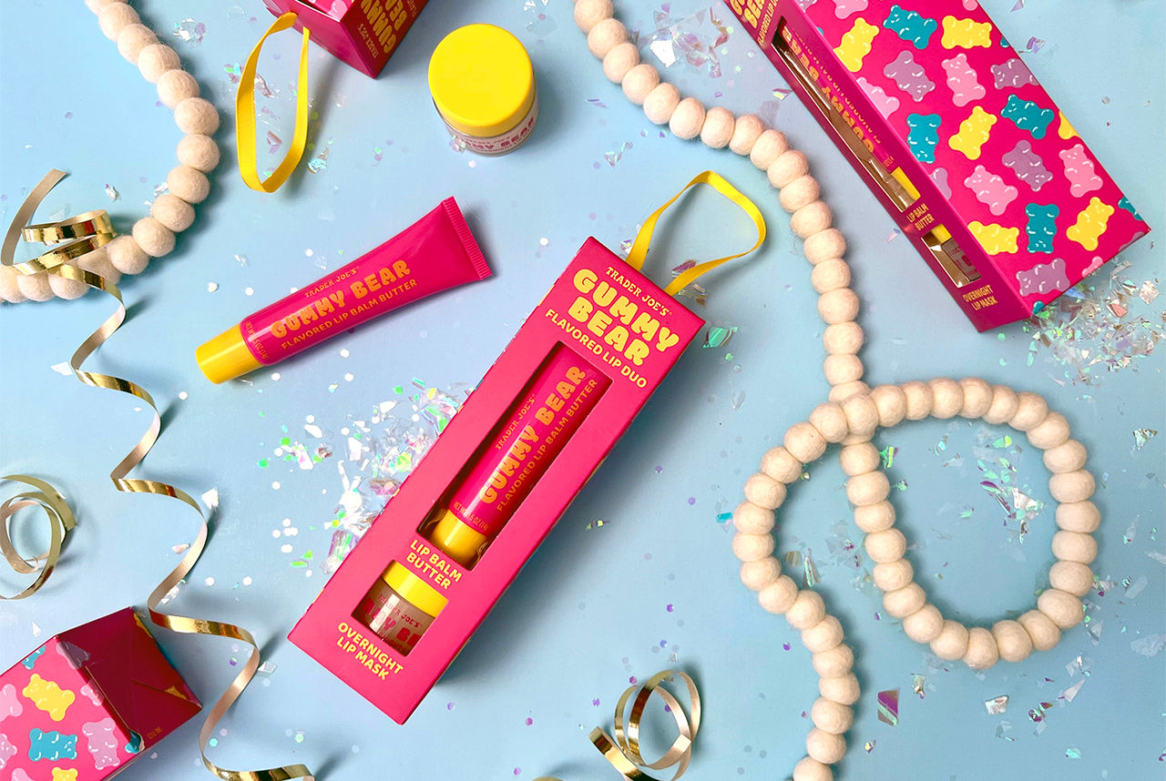 Several boxes of Trader Joe's Gummy Bear Flavored Lip Duo surrounded by confetti and holiday garlands