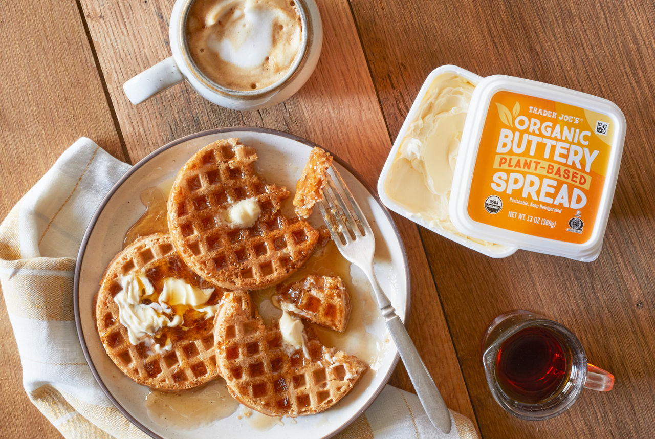 Trader Joe's Organic Buttery Plant-Based Spread; shown spread and melted on top of whole grain waffles with maple syrup; frothy coffee drink and maple syrup container in background