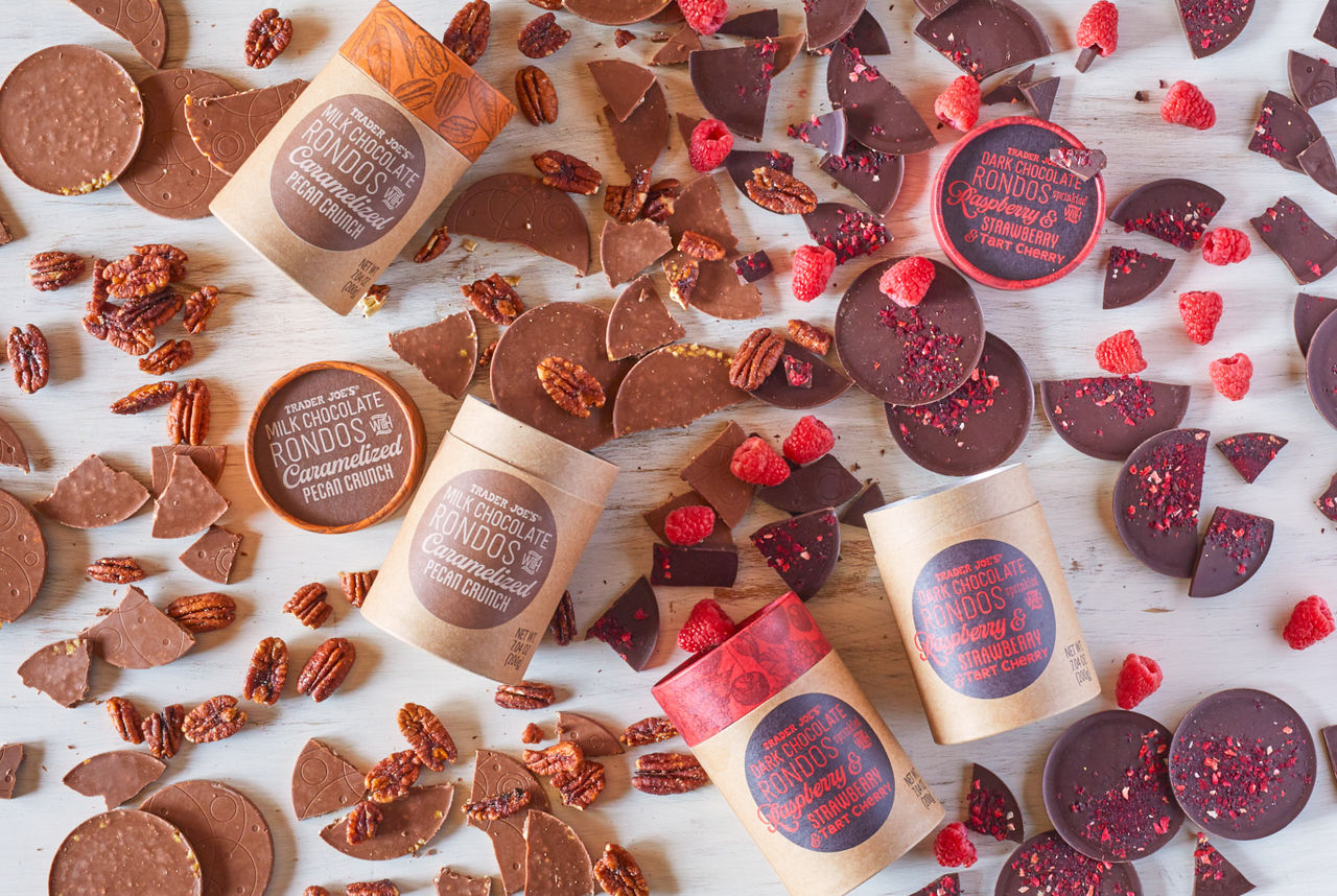 Trader Joe's Milk Chocolate & Dark Chocolate Rondos candy ; on white wood surface, many pieces surrounding containers, with pecans and fresh raspberries