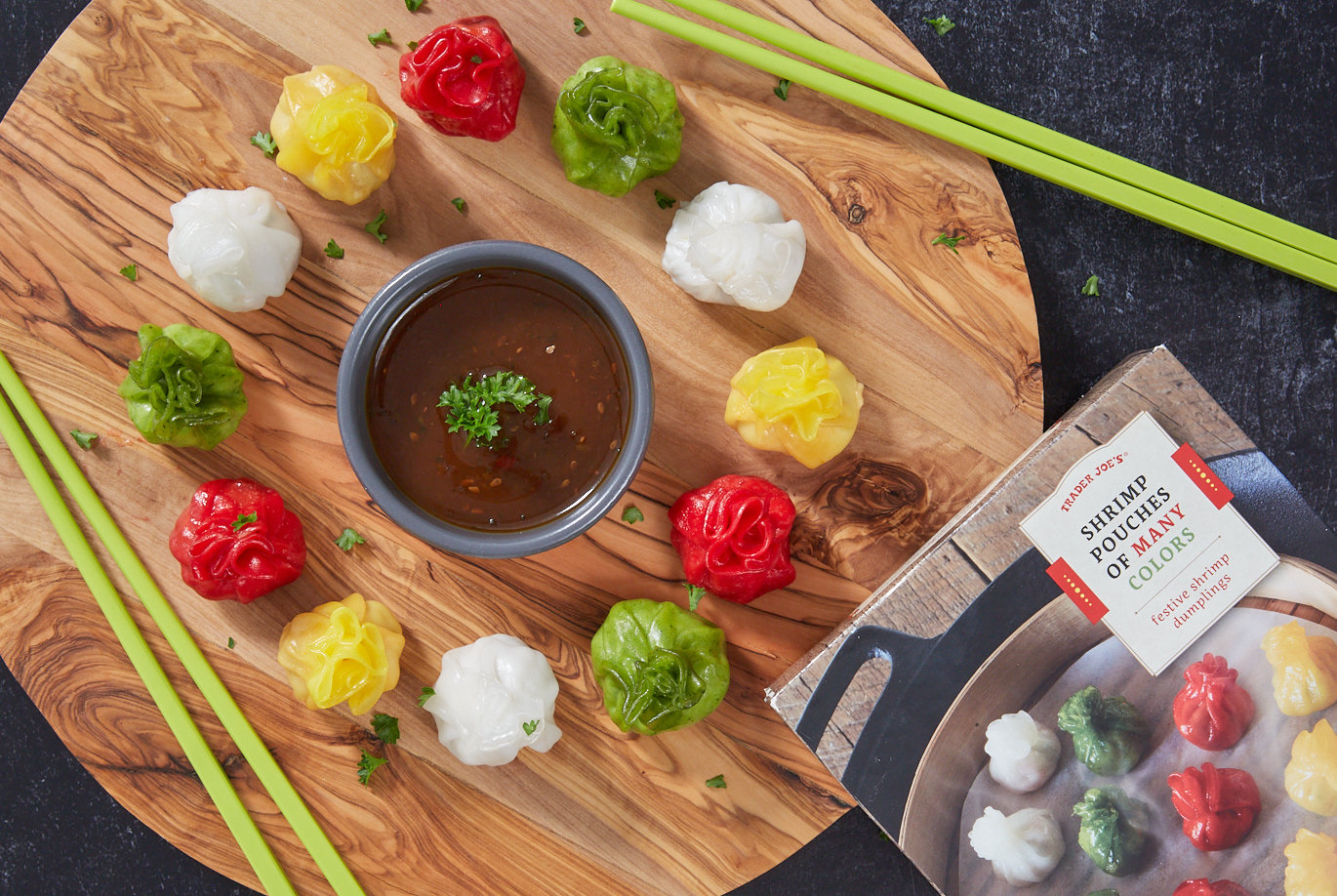 Trader Joe's Shrimp Pouches of Many Colors; shown arranged in a circle on circle wood board, small dish of dipping sauce in middle, 2 sets of chopsticks