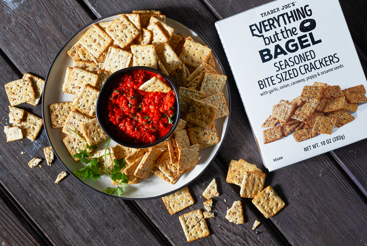 Trader Joe's Everything But The Bagel Seasoned Bite-Sized Crackers on a plate, with a small bowl of Red Pepper Spread in the middle