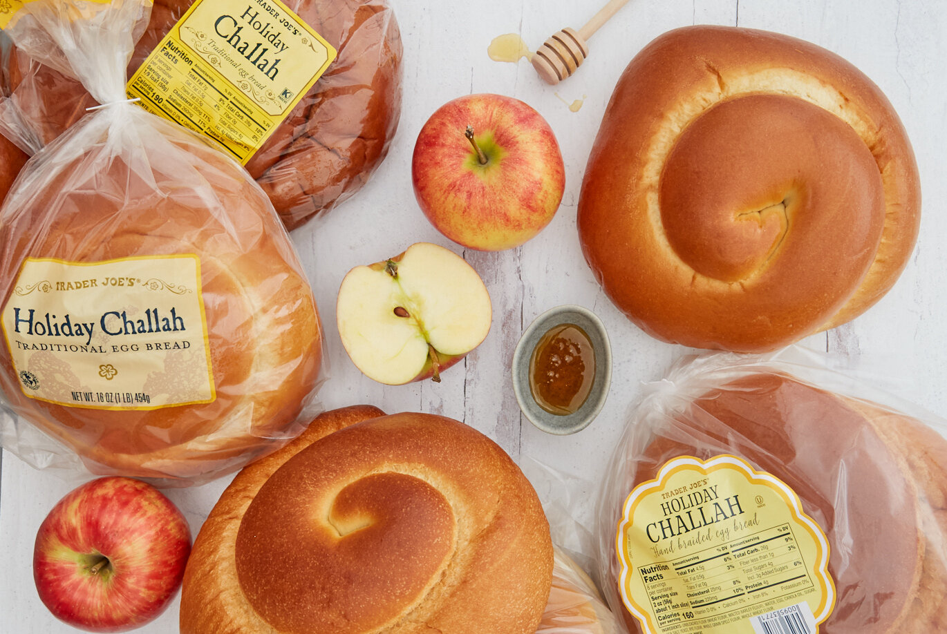 4 bags of Trader Joe's Holiday Round Challah offerings from regional suppliers; more whole challah out of bag and on surface with a dish of honey; whole apples and sliced apple half